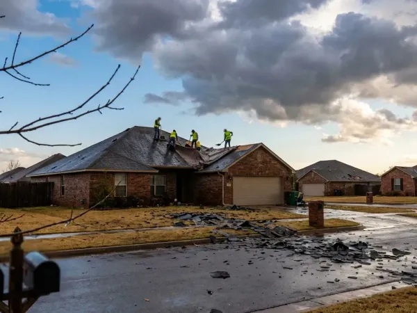 Roofing crew inspecting storm-damaged shingles on a residential home in Oklahoma City after a hail event