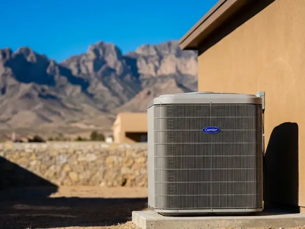 Professional HVAC technician servicing a condenser unit beside a stucco home in El Paso, TX, with the Franklin Mountains visible in the background