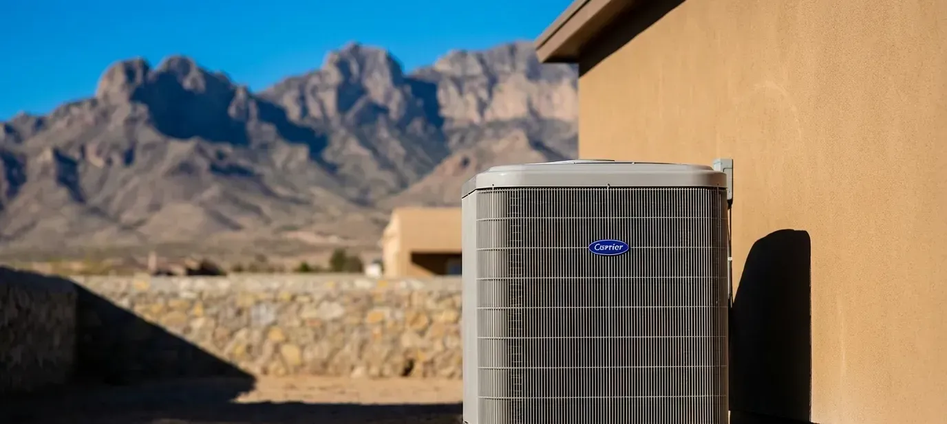 Professional HVAC technician servicing a condenser unit beside a stucco home in El Paso, TX, with the Franklin Mountains visible in the background