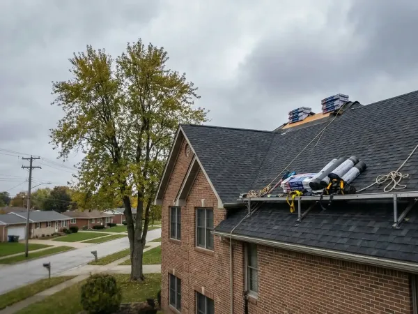 Professional roofing crew in safety gear inspecting a storm-damaged shingled roof on a suburban Omaha home under overcast Nebraska sky
