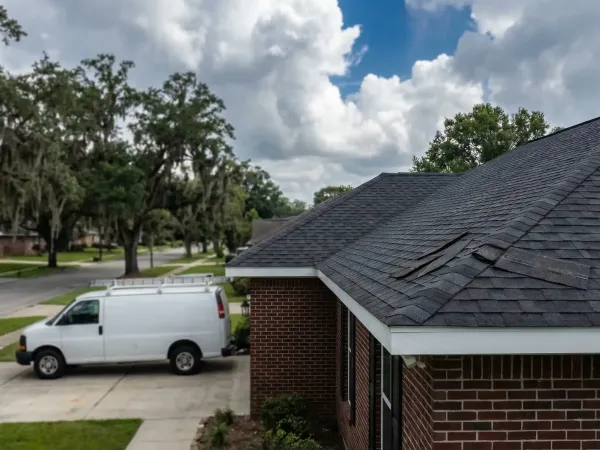 Roofing contractor inspecting storm damage on a residential home in Baton Rouge, LA with live oak trees in the background
