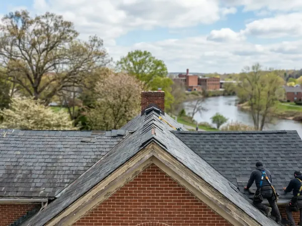 Professional roofing crew replacing steep-pitched roof on Grand Rapids, MI brick colonial home under spring Michigan sky