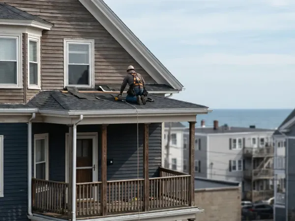 Professional roofing contractor installing shingles on a New Bedford, MA triple-decker residential building