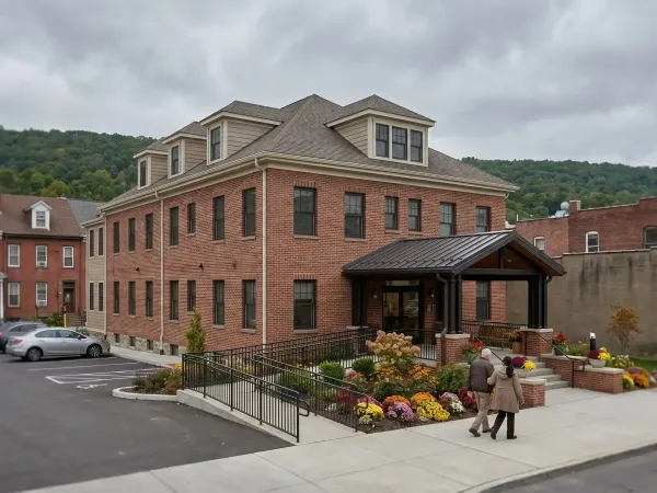 Caregiver and elderly resident walking together through the entrance of a brick senior care facility in Scranton, PA on a calm overcast afternoon
