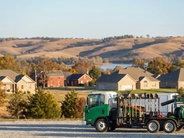 Professional landscaping crew member operating commercial lawn equipment on a striped residential yard in Rogers, AR with Ozark hills in the background